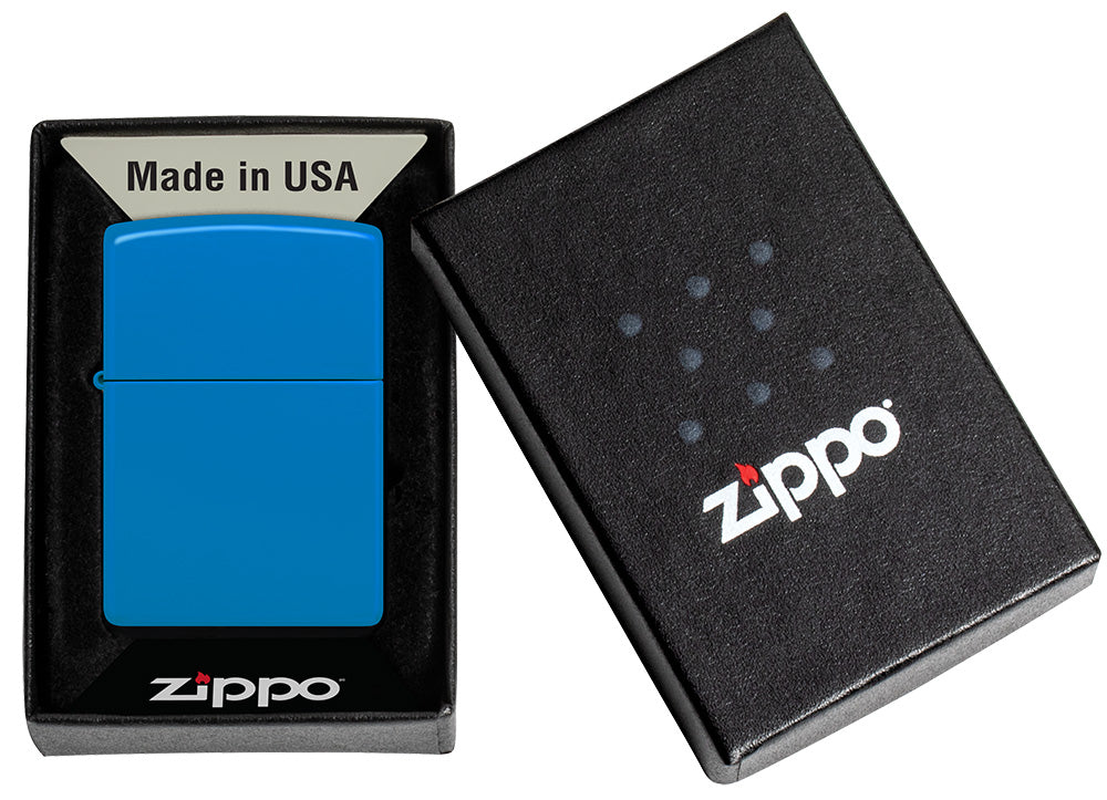 Ein blaues Zippo-Feuerzeug liegt in einer schwarzen Verpackung mit der Aufschrift "Made in USA", daneben der geschlossene Deckel mit Zippo-Logo.