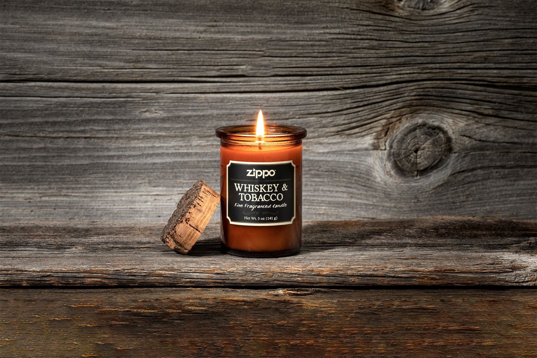 Zippo Kerze Whiskey und Tobacco braun mit Deckel aus Kork mit Flamme vor Holzhintergrund